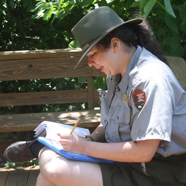 Park ranger in green and gray uniform writing in notebook
