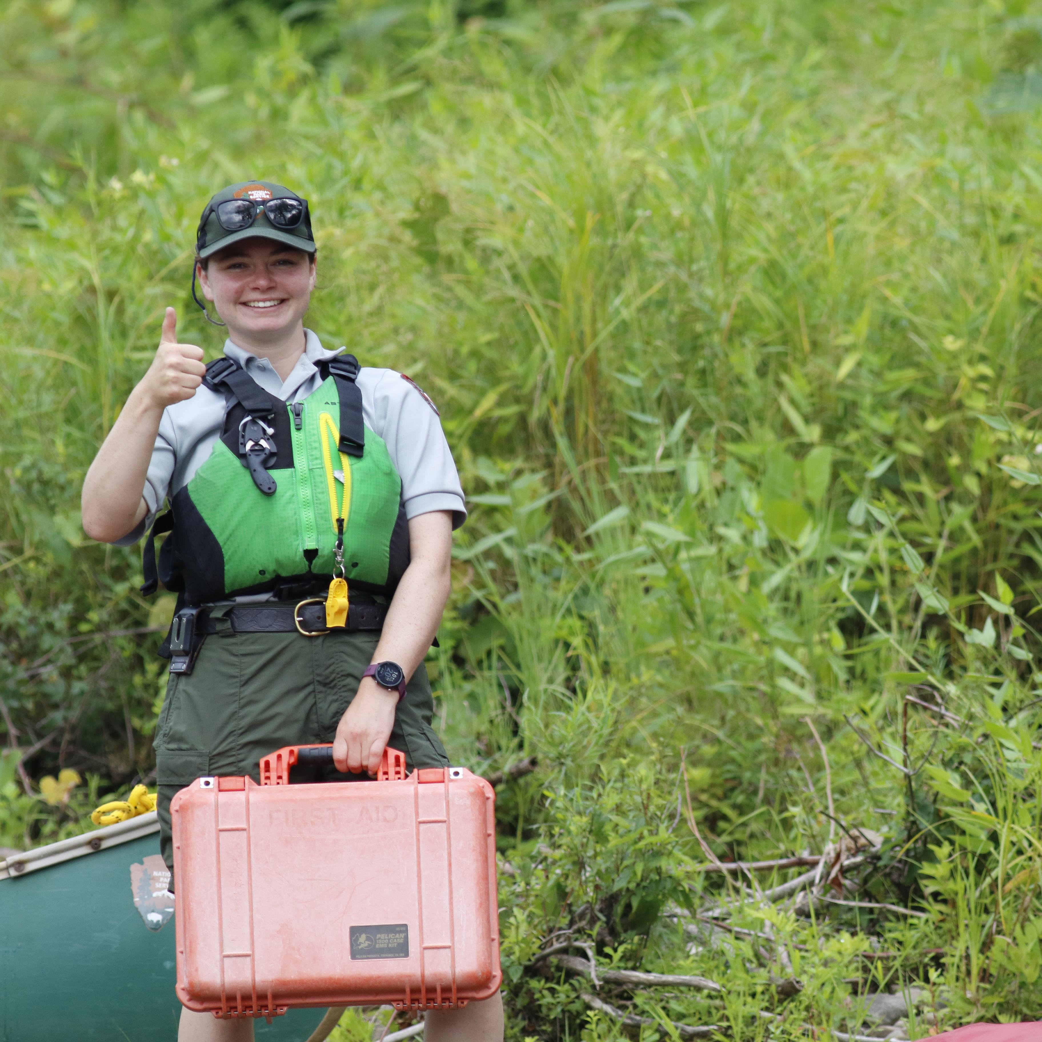 Park Ranger in life jacket smiles at camera while holding first aid kit.