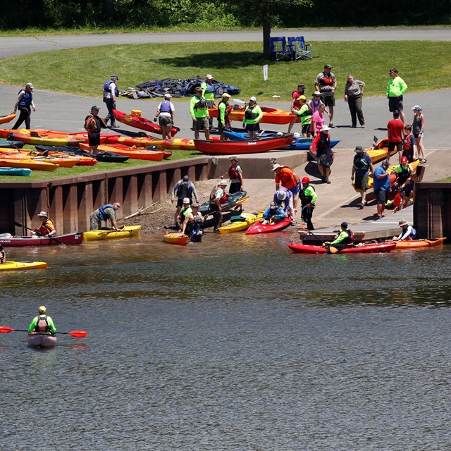 Public access area into a river. Paved ramp inclines into the river. People with kayaks enter water.