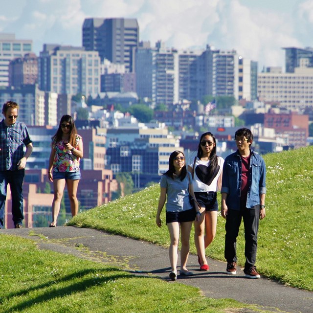 Park visitors walk on a paved trail in an urban park.