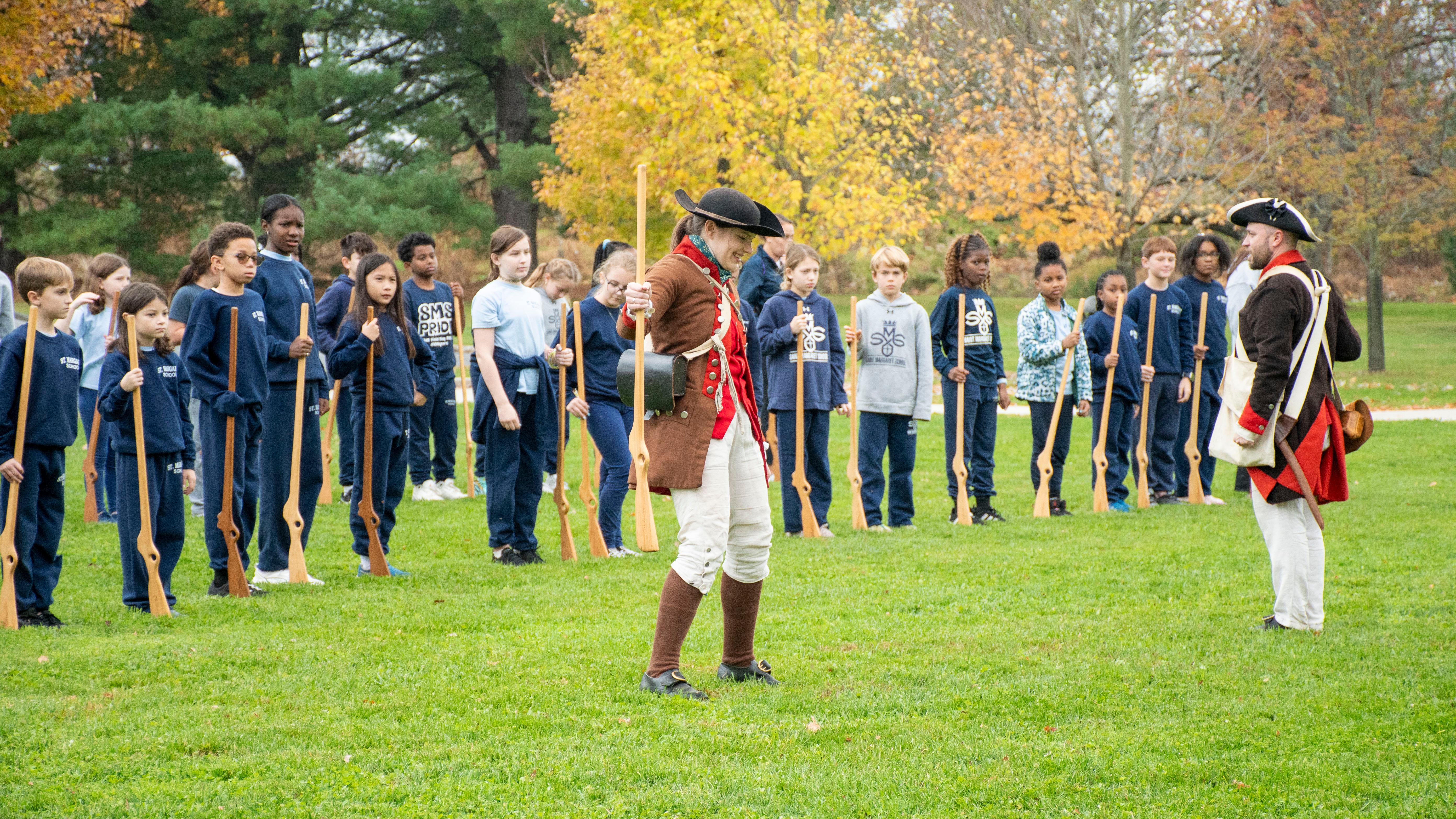 students in school uniforms hold wooden muskets in the air to mimic park rangers in soldier uniforms