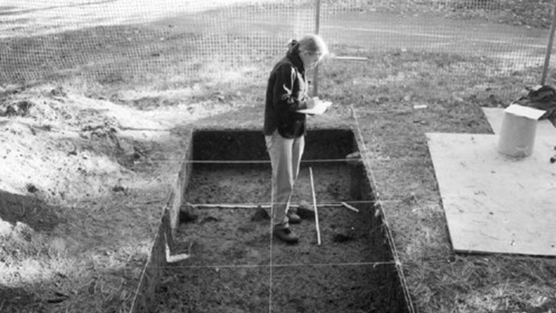 Black and white photograph of a person standing in an excavation pit.