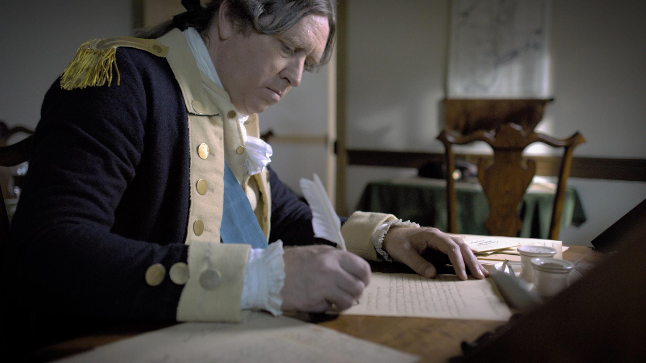 General George Washington sits and writes at a desk.