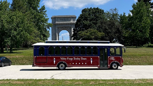 A red and blue trolley in front of large arch monument