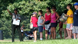 outdoors, grass, trees, ranger speaking to a group and pointing