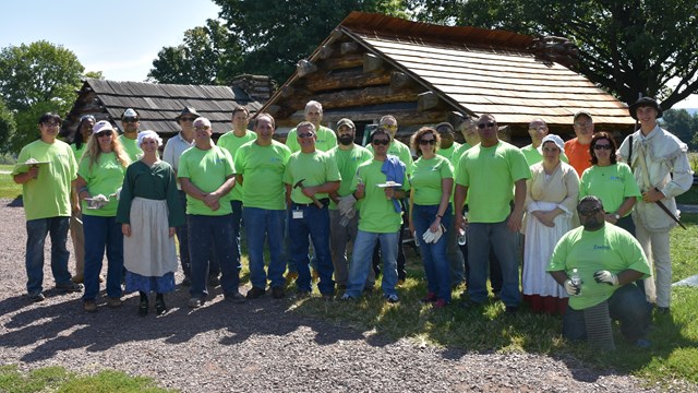A group of people in matching company t-shirts stand in front of a hut.