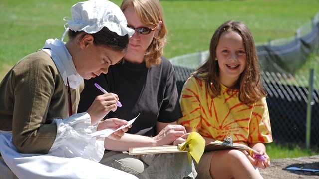 A young woman in colonial clothing helps visitors unravel clues in a mystery.