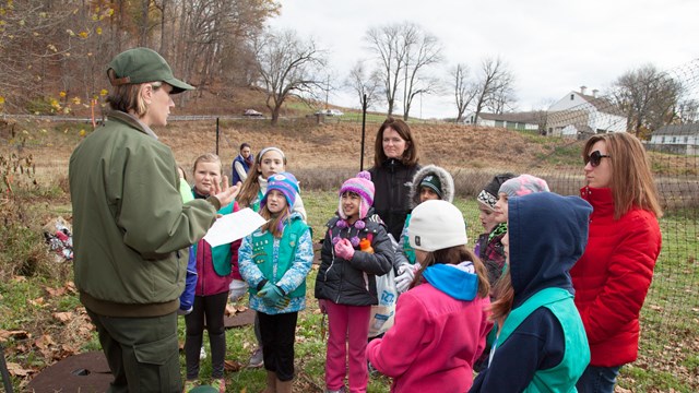 A park ranger speaks to a group of young girls in Girl Scout uniforms.