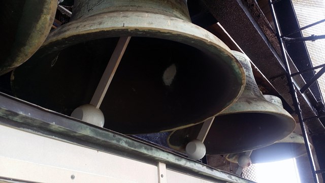 Large bells in a row in a bell tower interior.