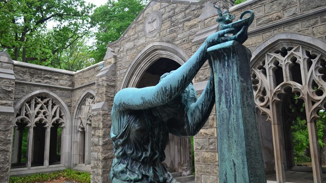 A stone statue of a woman holding a lamp up on a pedestal.