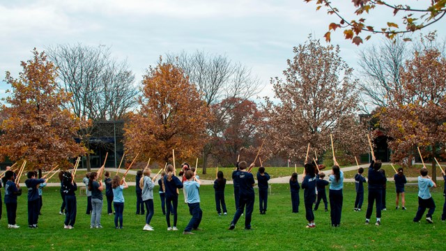 students in school uniforms hold wooden muskets in the air to mimic park rangers in soldier uniforms