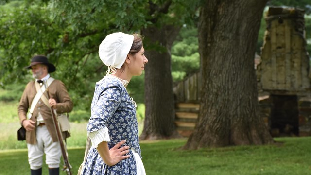 A woman in a blue gown stands in front of a soldier.