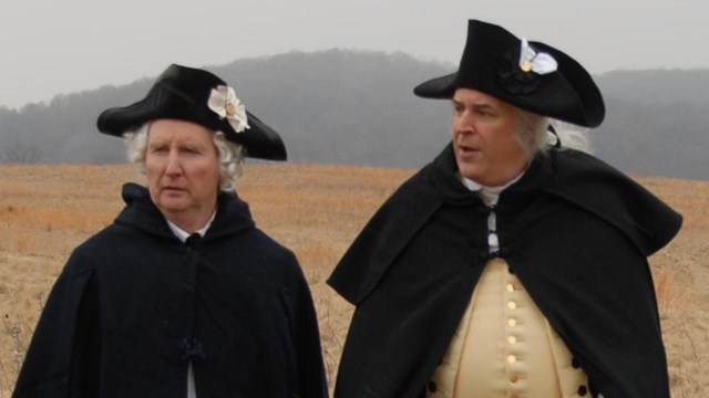 Group of 18th century men standing in a field during an overcast day.