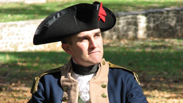 Young Continental Army officer sitting behind field desk. 