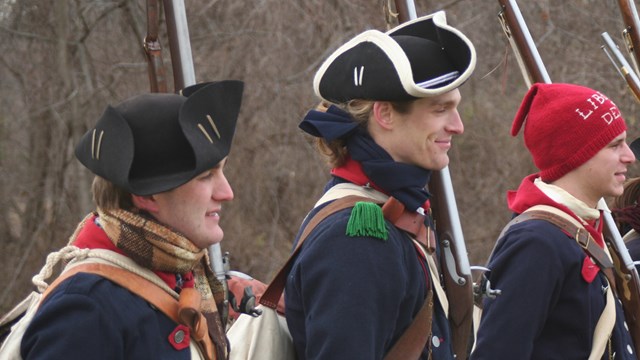 Continental soldiers shoulder to shoulder hold musket against left side of body. 