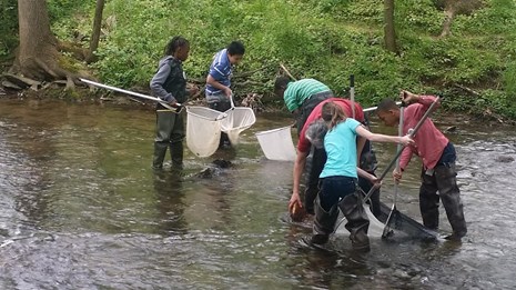 A group of children stand in a creek holding nets.