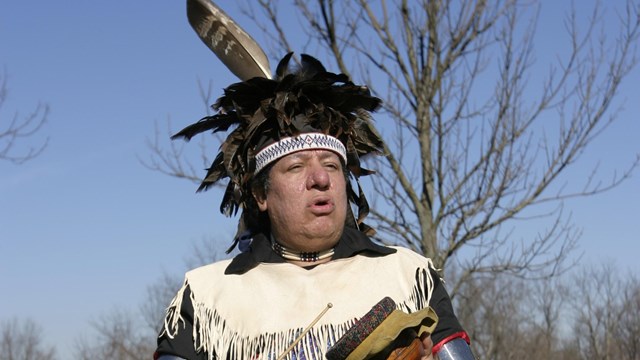 Oneida warrior wearing blue traditional garb with drum in hand.
