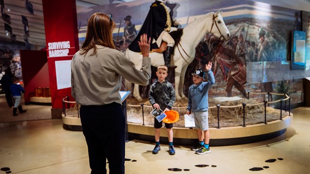 two children stand in front of a statue of George Washington on a horse with their hands raised