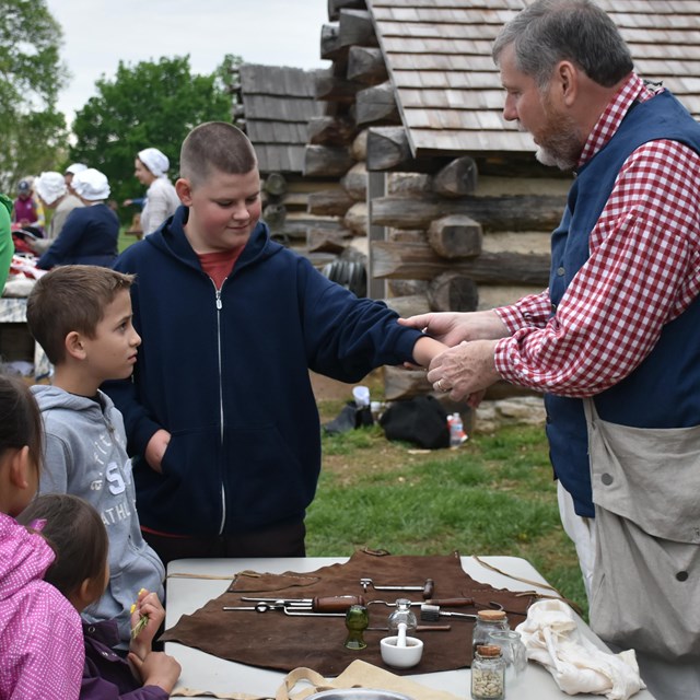 Man demonstrating 18th Century medical tools on student. 