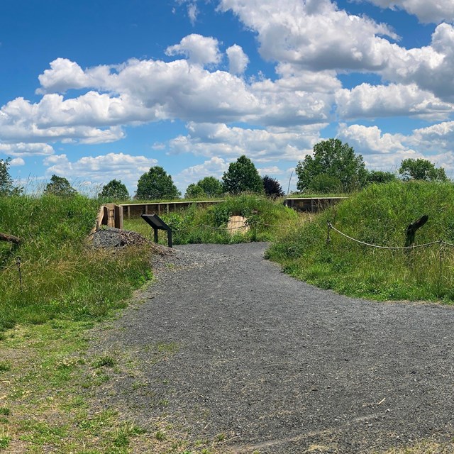 grass covered mound with pointed logs facing outwards and an entrance path