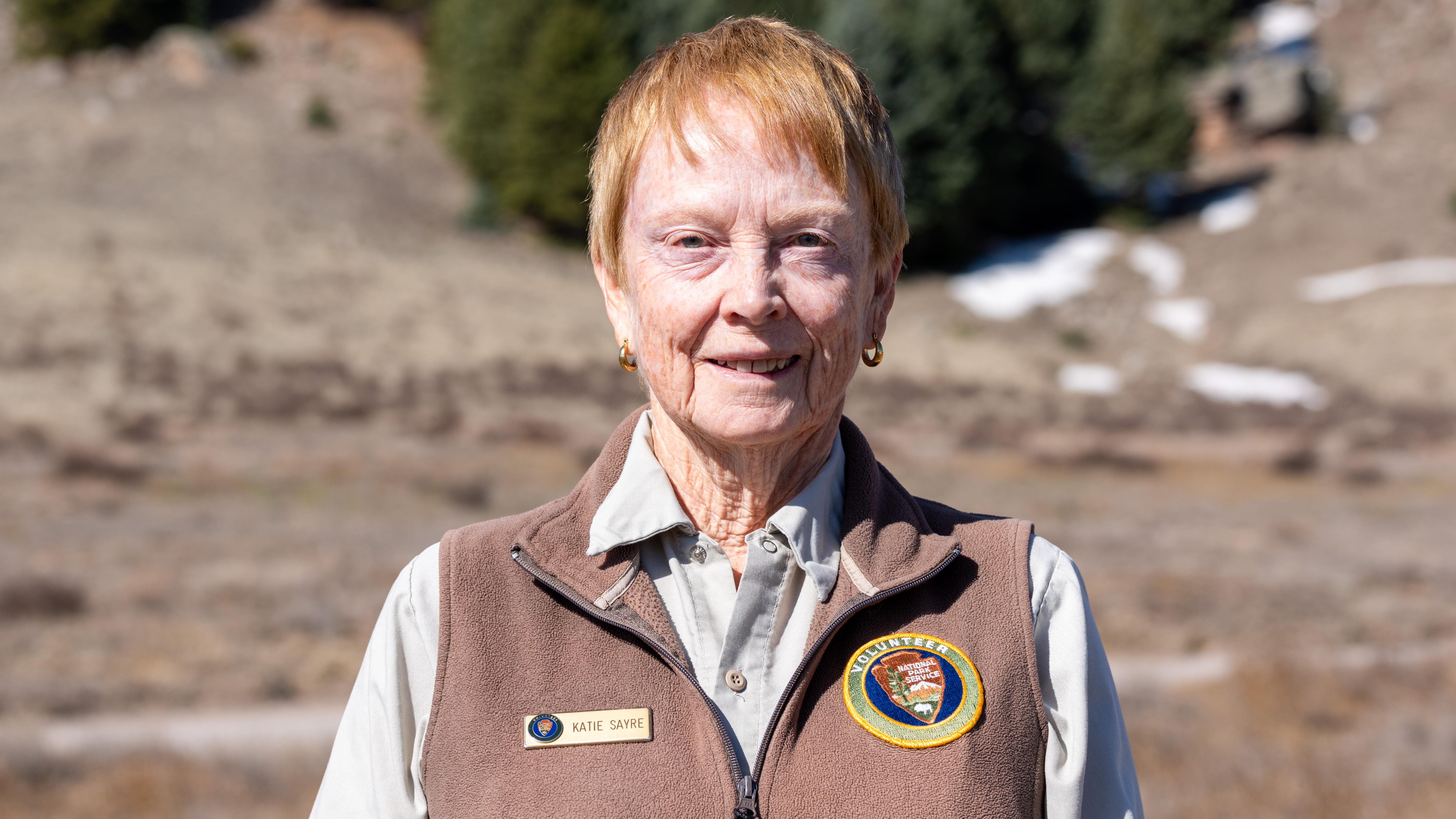 A park volunteer wearing a brown uniform vest over a khaki shirt smiles at us.
