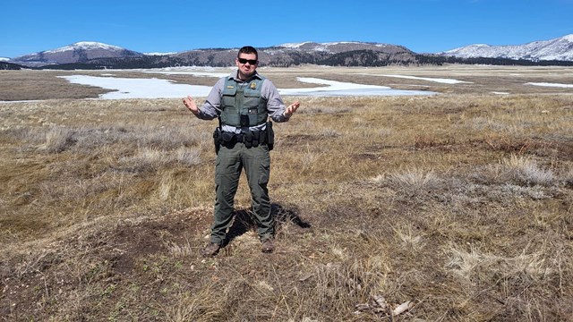 A park ranger stands in a valley with patchy snow.