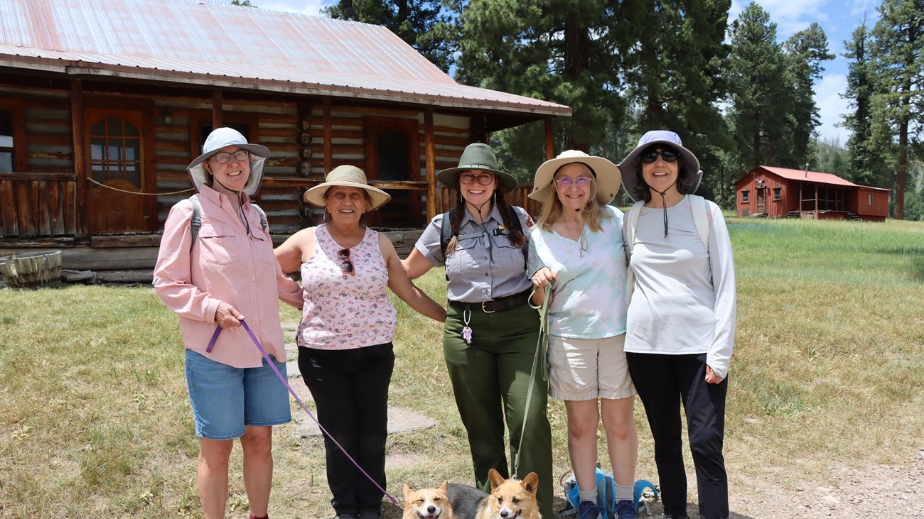 A group of program participants, including two leashed dogs, smile alongside a park ranger.