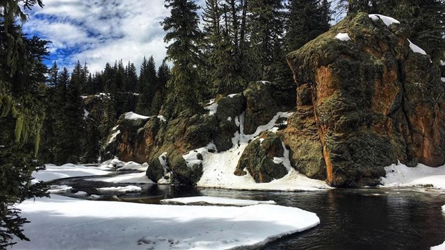 A small, icy stream flows through a snowy valley