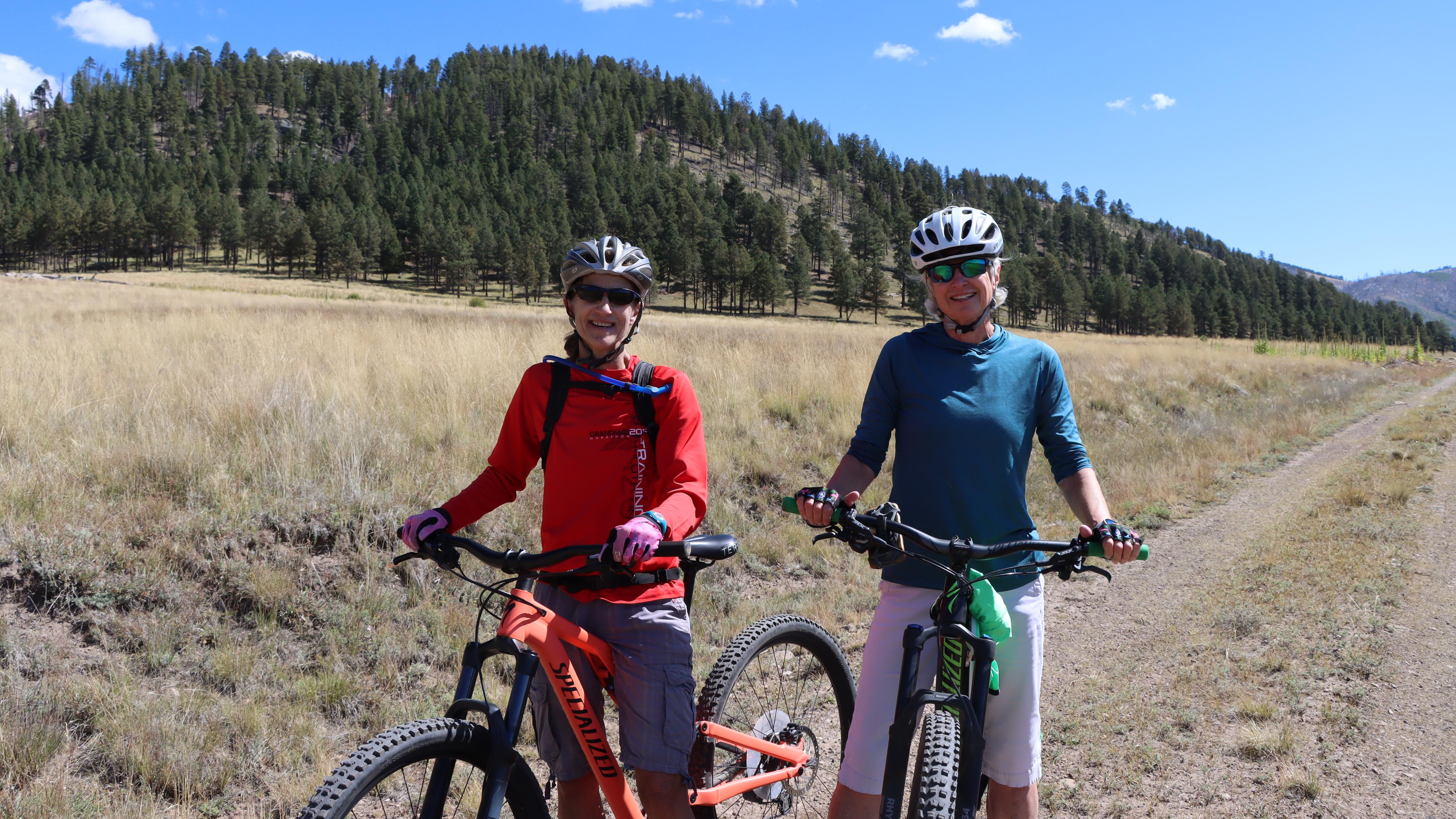 Two cyclists wearing sunglasses and helmets stand with their bikes.
