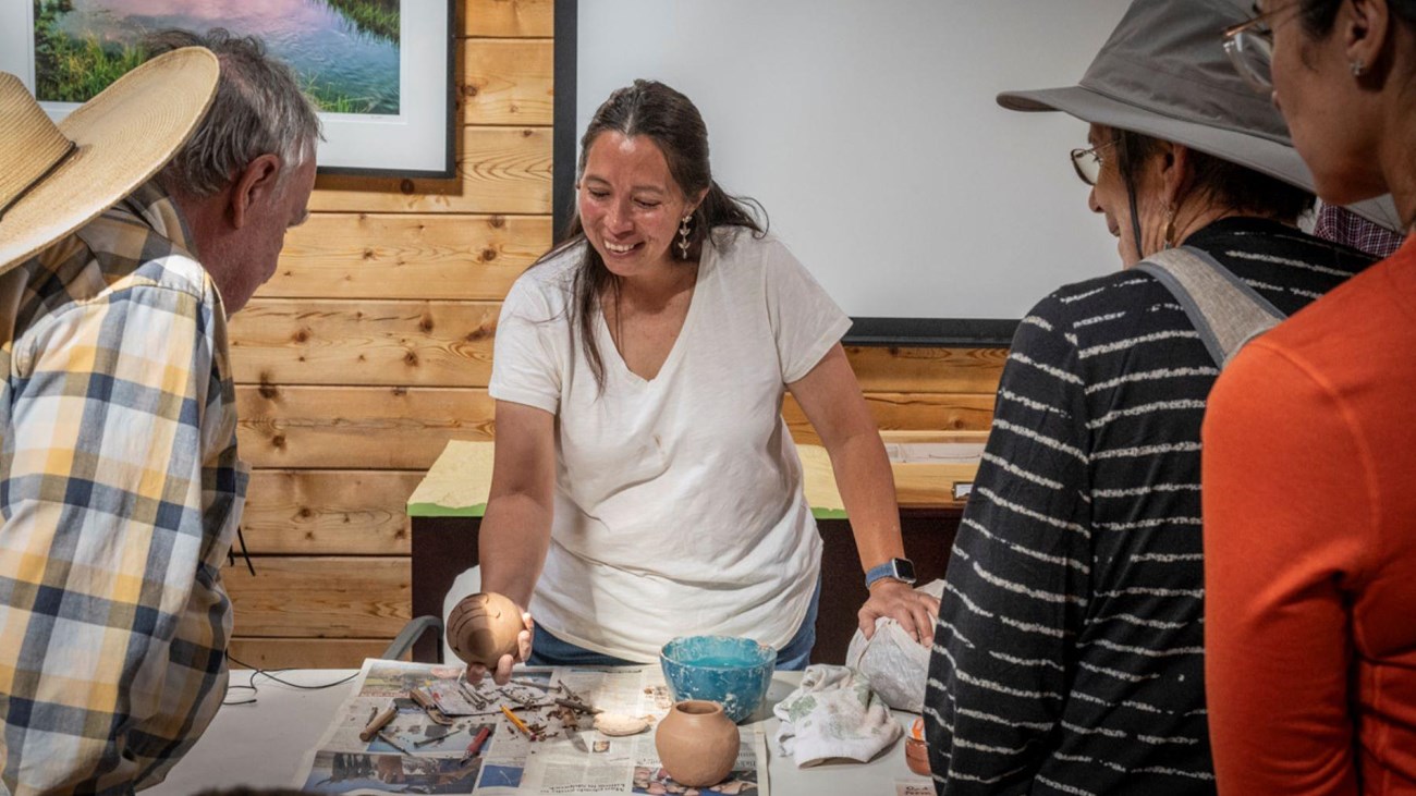 A woman shows her handmade pottery to three onlookers. 