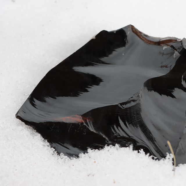 A smooth piece of black, transparent rock in the snow.
