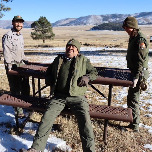 Three National Park Service employees laugh as they move a picnic table.