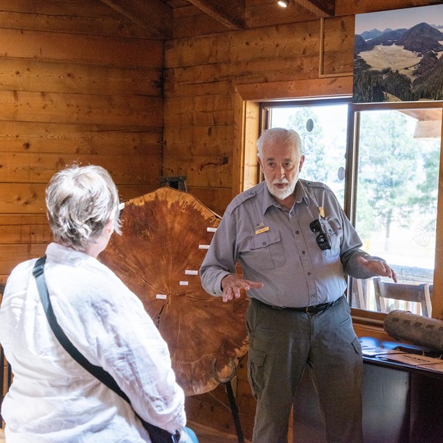 Two visitors ask a park ranger a question inside a wooden building