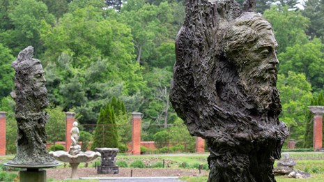 Two bronze head and shoulder sculptures of men set within a garden.
