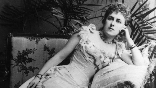 A black and white photograph of a reclining woman wearing a gown and holding a fan.
