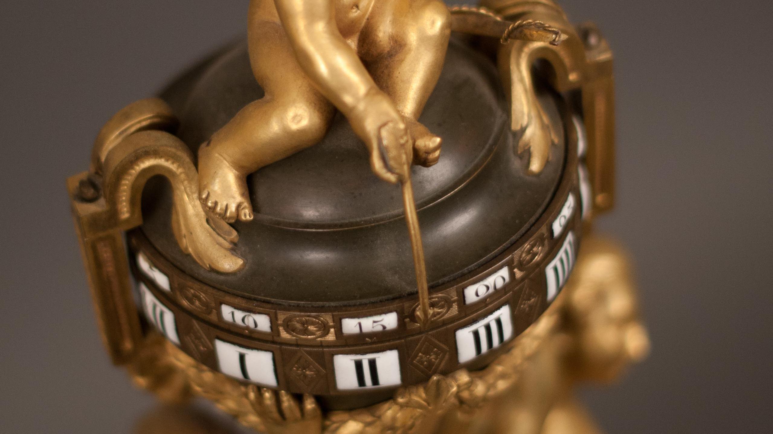A clock with gilt putti pointing an arrow at the time. 