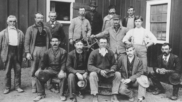 A black and white photo of a group of men standing in front of a building.