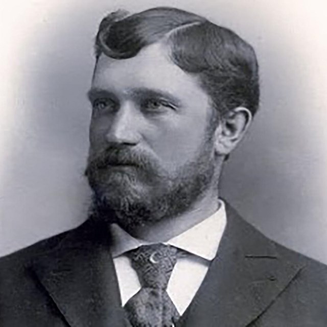 A black and white portrait of a man with beard wearing a suit.