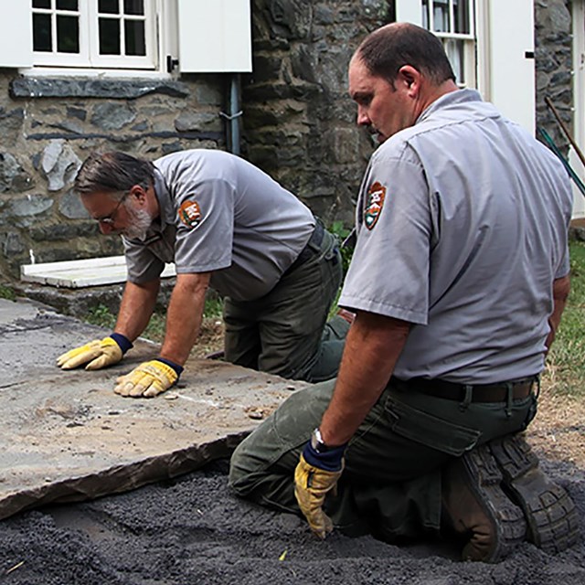 Two park rangers set slabs of bluestone along a path.