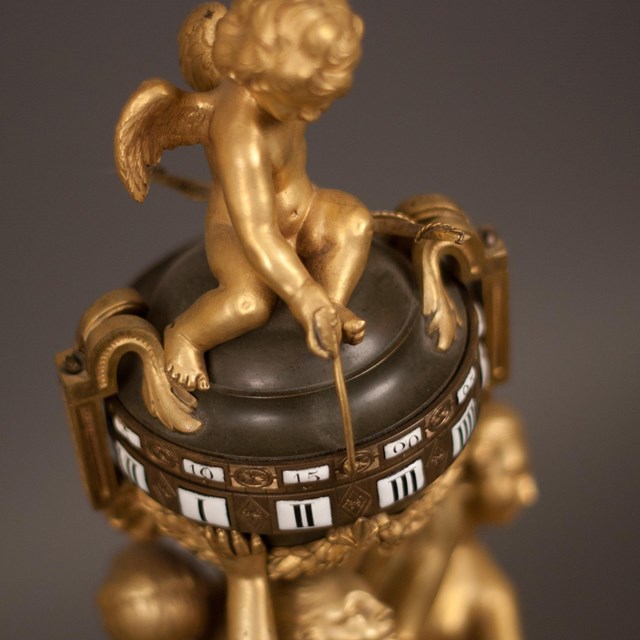 A clock with gilt putti pointing an arrow at the time. 