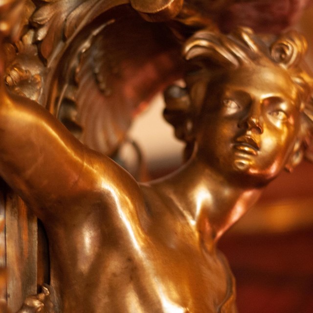 Detail of a gilt male figure mounted to a marble fireplace.