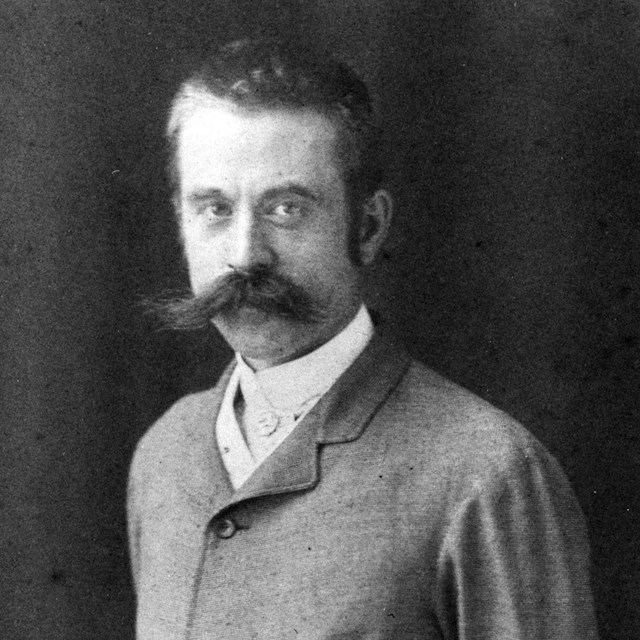A main with a large mustache wearing a suit.