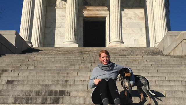 A woman and dog sitting on the stairs leading up inside the Illinois monument's rotunda.