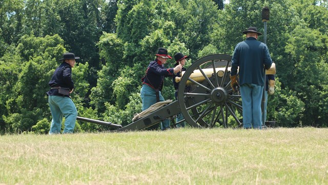 A group of people in Civil War uniforms standing around a cannon.