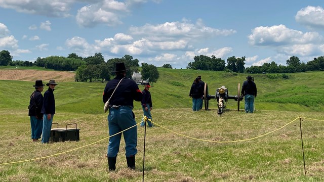 Volunteers in Civil War uniforms standing around a cannon during Fourth of July.
