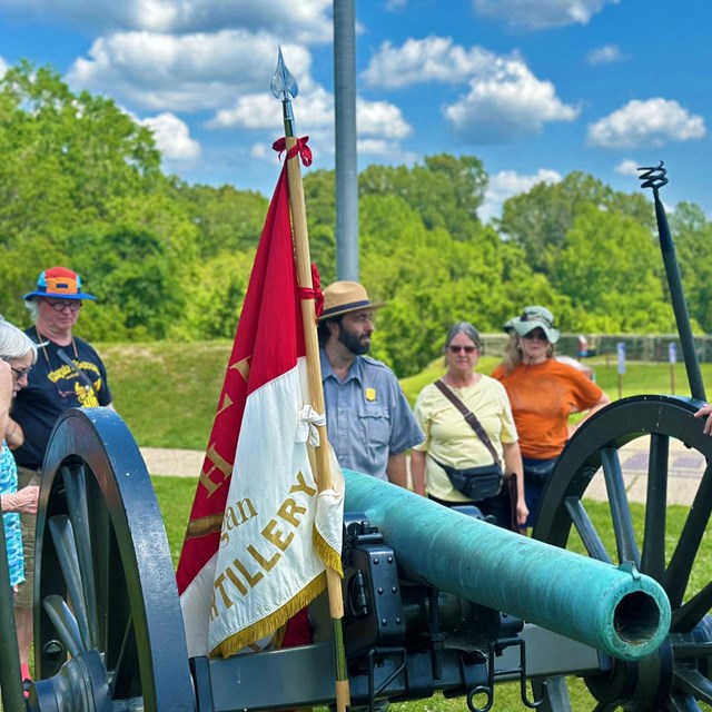 A Park Ranger speaks to a group of visitors next to a cannon.