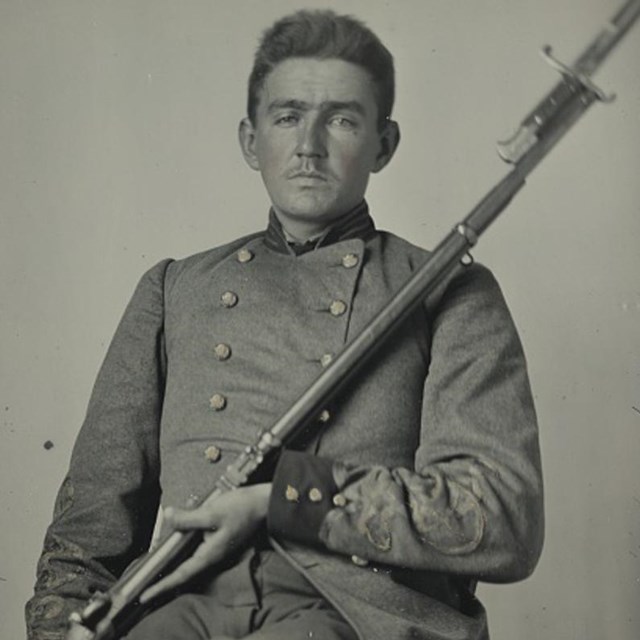 A Confederate soldiers from Arkansas in gray uniform holding a musket with a bayonet attached