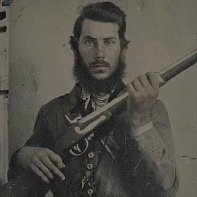 A Confederate soldier in gray uniform holding his musket in front of his body