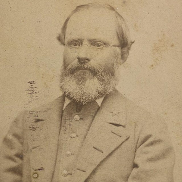 A Confederate officer with gray jacket opened wearing glasses