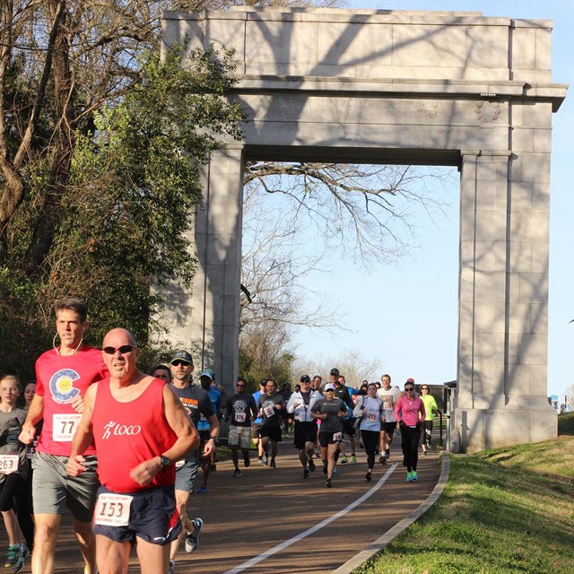 A group of runners passing through the Memorial Arch on the park tour road.